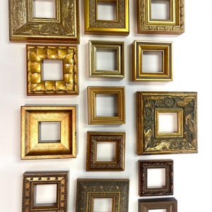 May include: A collection of ornate, square picture frames in various sizes and finishes. The frames are primarily gold and brown, with detailed carvings and textures. The arrangement showcases a variety of styles, from simple to highly decorative.