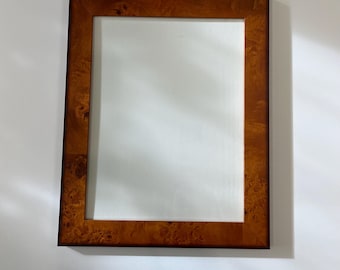 May include: Rectangular mirror with a dark brown, burr wood frame. The frame has a rich, warm tone with a natural wood grain pattern. The mirror is mounted on a white wall, and the frame's edges are clean and well-defined.