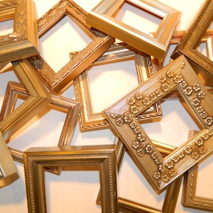 以下が含まれることがあります： さまざまなサイズとスタイルの金色の写真フレームのコレクションで、いくつかは装飾的なデザインが施されています。フレームはランダムなパターンで配置され、互いに重なっています。