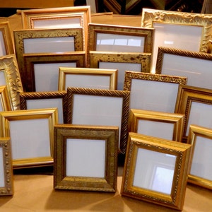 Puede incluir: Una colección de varios marcos de fotos cuadrados y rectangulares en tonos dorados, bronce y metálicos. Cada marco cuenta con un paspartú blanco y muestra una variedad de texturas decorativas, tallas ornamentadas y acabados lisos.