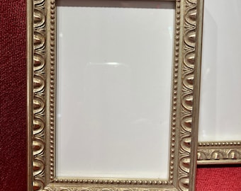 Può includere: Una cornice per foto argentata con un design ornamentale. La cornice ha un passepartout bianco ed è pronta per esporre una foto o un'opera d'arte.