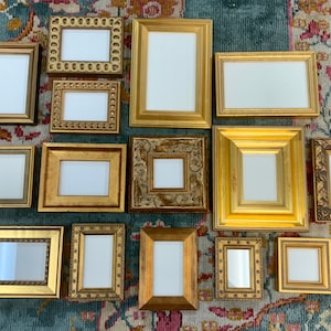 以下が含まれることがあります： 様々なサイズとスタイルの13個の金色の写真フレームが、模様のある敷物の上に並んでいます。フレームはすべて空で、写真やアート作品を飾る準備ができています。