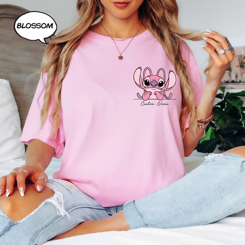 Pu&ograve; includere: T-shirt rosa chiaro con un disegno di personaggio dei cartoni animati. Il disegno &egrave; un alieno rosa con grandi orecchie e occhi, con la scritta "Custom Name" sotto. La parola "BLOSSOM" &egrave; in una nuvoletta in alto a sinistra.