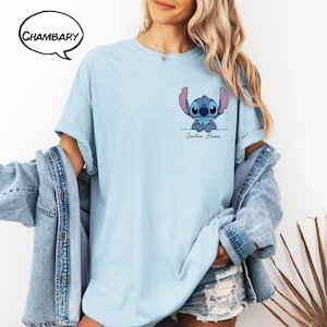 Pu&ograve; includere: T-shirt azzurra con un'immagine a cartoni animati di Stitch e la scritta "Custom Name" sotto. La maglietta ha maniche corte e una vestibilit&agrave; ampia. Il marchio "Chambary" &egrave; in un fumetto nell'angolo in alto a sinistra.