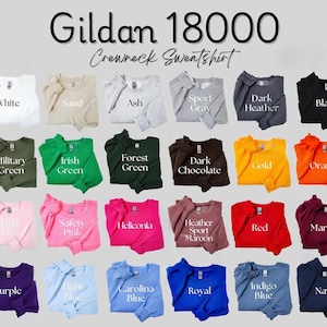 Pu&ograve; includere: Una vetrina di felpe girocollo Gildan 18000 in vari colori, tra cui bianco, nero e blu navy. L'immagine mostra una gamma di tonalit&agrave;, dal rosa chiaro al cioccolato fondente, con il nome di ogni colore visualizzato sotto.