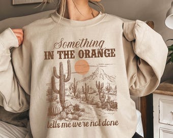 カントリーミュージック愛好家へのギフト、ウエスタンコンサートスウェットシャツ、ロデオTシャツ、カウボーイ衣装、オレンジの中にある何かがまだ終わっていないことを教えてくれるシャツ