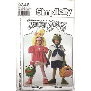 May include: Simplicity sewing pattern for Muppet Babies costumes. The pattern features instructions for Miss Piggy and Kermit costumes. The Miss Piggy costume includes a pink dress and a pig-shaped headpiece. The Kermit costume includes a sailor shirt and a frog-shaped headpiece.