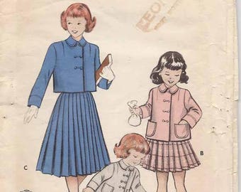 May include: Vintage Butterick printed patterns envelope featuring illustrations of children's clothing. The designs include a blue pleated skirt and jacket, a pink jacket and skirt, and a gray jacket and skirt. The envelope has text that reads "PRINTED PATTERNS".
