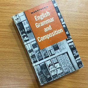 Puede incluir: Un ejemplar antiguo del libro "Warriner's English Grammar and Composition". El libro tiene una cubierta desgastada con un bloque de título naranja y un diseño en blanco y negro. El título está impreso en blanco.