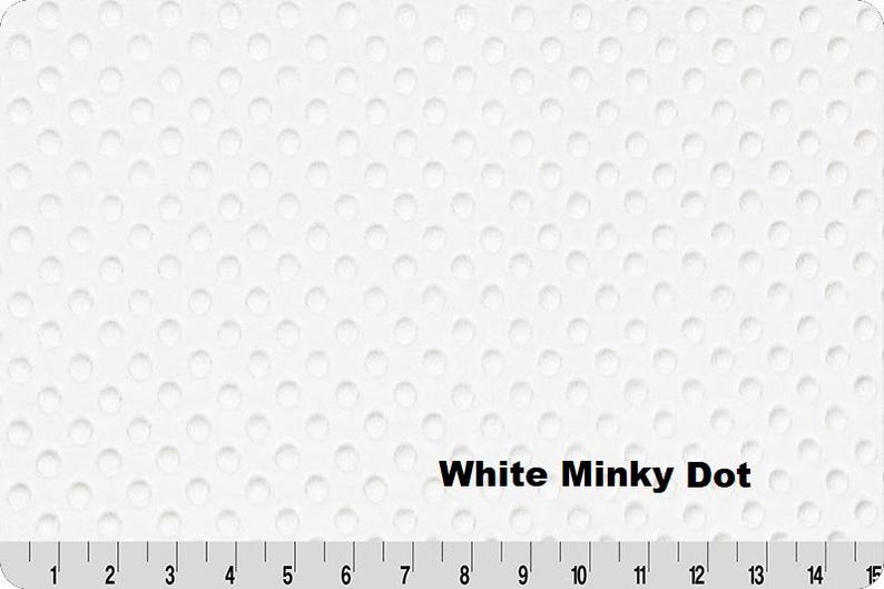 Pu&ograve; includere: Tessuto bianco a pois minky con superficie strutturata. Il tessuto presenta un motivo di piccoli punti in rilievo distanziati uniformemente. Il testo "White Minky Dot" &egrave; visualizzato sul tessuto. Un righello &egrave; nella parte inferiore dell'immagine, con misure in centimetri.