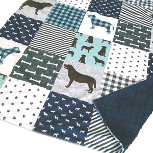 May include: A patchwork quilt featuring a variety of square fabric patterns in shades of navy blue, light blue, gray, and white. The design includes repeating motifs of dog silhouettes, paw prints, bones, and plaid patterns, with a dark blue textured backing.