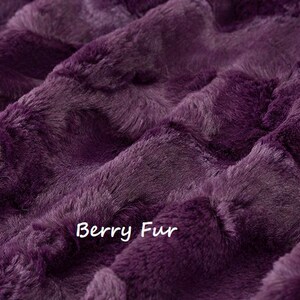 Puede incluir: Primer plano de una tela de felpa de color morado oscuro. La tela tiene una textura suave y peluda y un patr&oacute;n ligeramente acolchado. El texto "Berry Fur" est&aacute; impreso en la tela.
