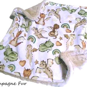 May include: A white baby blanket with a pattern of watercolor dragons in shades of green, brown, and tan. The blanket has a soft, champagne-colored fur trim and the text "Champagne Fur" at the bottom.