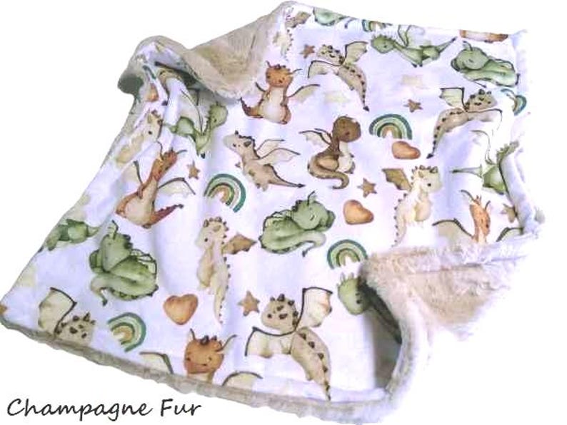 May include: A white baby blanket with a pattern of watercolor dragons in shades of green, brown, and tan. The blanket has a soft, champagne-colored fur trim and the text "Champagne Fur" at the bottom.