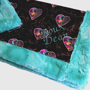 Pu&ograve; includere: Una coperta per bambini turchese e nera con un motivo a cuore e il nome "Roux Dean" ricamato in turchese. La coperta ha un bordo morbido e felpato turchese.