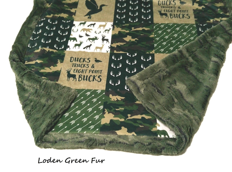 May include: A green and brown patchwork blanket with a soft, green fur trim. The blanket features squares with camouflage, deer silhouettes, arrows, and the text "DUCKS TRUCKS & EIGHT POINT BUCKS". The text "Loden Green Fur" is at the bottom.