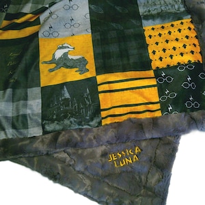 May include: A patchwork blanket with a gray faux fur border. The blanket features squares with various designs, including glasses, lightning bolts, and a badger. The name "JESSICA LUNA" is embroidered in gold thread on the border.