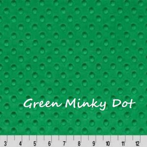 May include: A vibrant green minky fabric featuring a raised, embossed dot pattern across the entire surface. The text "Green Minky Dot" is printed in white in the center. A white ruler with black markings from 1 to 15 inches is at the bottom.