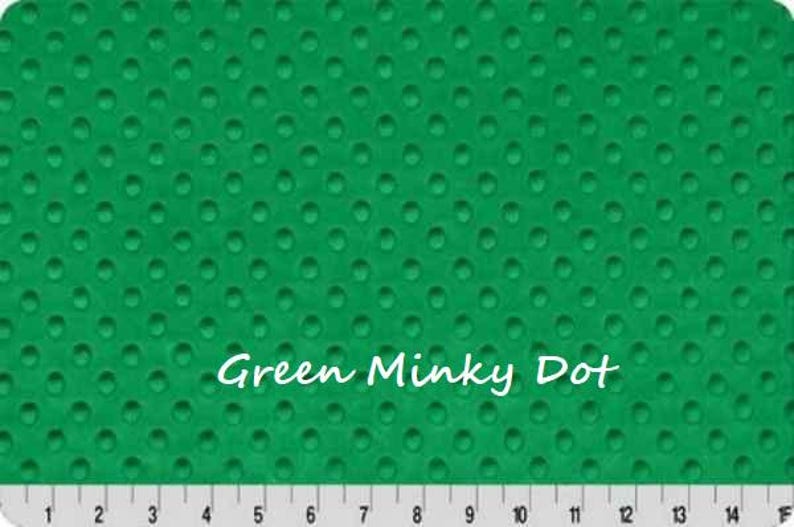 May include: A vibrant green minky fabric featuring a raised, embossed dot pattern across the entire surface. The text "Green Minky Dot" is printed in white in the center. A white ruler with black markings from 1 to 15 inches is at the bottom.