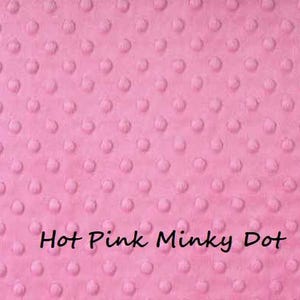 Pu&ograve; includere: Un tessuto rosa acceso a pois minky con una superficie strutturata. Il tessuto presenta un motivo di piccoli pois in rilievo distribuiti uniformemente sulla superficie. Le parole "Hot Pink Minky Dot" sono scritte in nero.