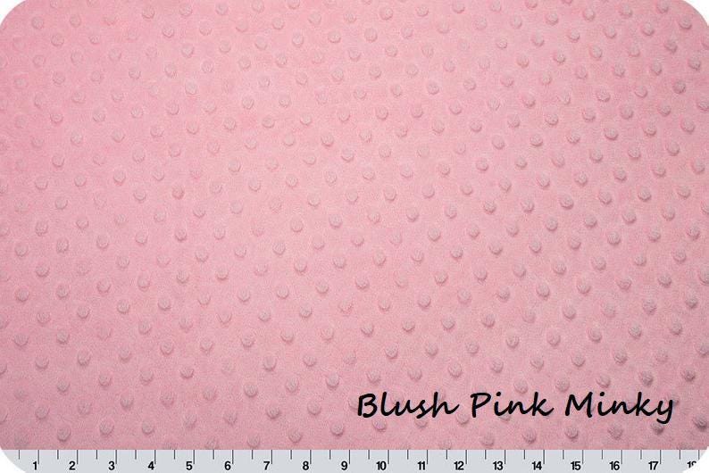 May include: Blush pink minky fabric with a textured, dotted pattern. The fabric is a soft, light pink color and has a plush feel. The text "Blush Pink Minky" is written in a cursive font across the bottom of the fabric.