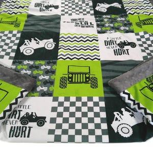 May include: A patchwork quilt featuring a jeep theme with green, white, and gray squares. The quilt has a gray minky backing and includes text that reads "A little dirt never hurt" and "Yours may go fast, I can go anywhere."