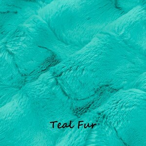 May include: Close-up of teal-colored faux fur fabric. The plush material has a textured, rippled appearance with visible fibers. The words "Teal Fur" are printed in black at the bottom of the image.