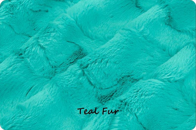 May include: Close-up of teal-colored faux fur fabric. The plush material has a textured, rippled appearance with visible fibers. The words "Teal Fur" are printed in black at the bottom of the image.
