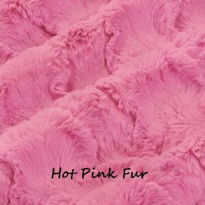 Pu&ograve; includere: Primo piano di un tessuto in finta pelliccia rosa acceso. Il materiale in peluche ha un aspetto strutturato e ondulato. Le parole "Hot Pink Fur" sono stampate in nero nella parte inferiore dell'immagine.
