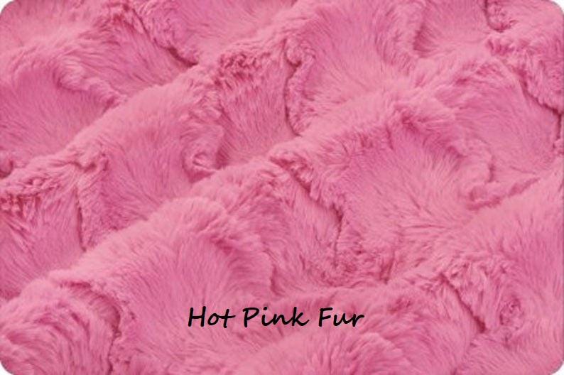 Pu&ograve; includere: Primo piano di un tessuto in finta pelliccia rosa acceso. Il materiale in peluche ha un aspetto strutturato e ondulato. Le parole "Hot Pink Fur" sono stampate in nero nella parte inferiore dell'immagine.