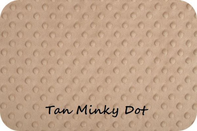 May include: Tan-colored minky dot fabric with a rounded rectangular shape. The fabric has a soft, textured surface with evenly spaced, raised dots. The words "Tan Minky Dot" are written in a cursive font at the bottom of the fabric.
