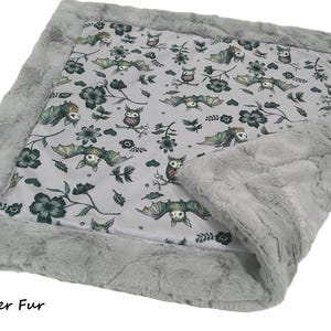 May include: A rectangular blanket featuring a light gray center panel with a repeating pattern of bats, owls, and dark green flowers. The blanket is bordered by a thick, textured silver faux fur trim. The text Silver Fur is visible.