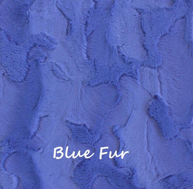 May include: A vibrant blue faux fur fabric featuring a textured, swirling pattern throughout the material. The surface displays a dense, soft pile with varying light and shadow effects across the fibers. The text Blue Fur is printed in white.