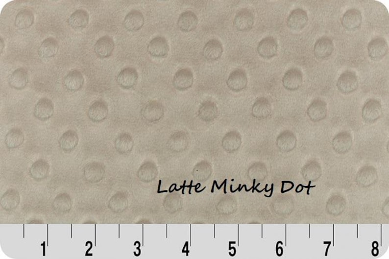 May include: Close-up of a beige Latte Minky Dot fabric. The fabric has a soft, textured surface with evenly spaced, raised dot patterns. The image includes a ruler along the bottom, showing measurements in inches.