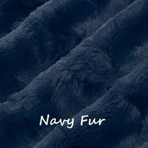 May include: Close-up of navy blue faux fur fabric. The plush material has a soft, textured appearance with visible fibers and folds. The words "Navy Fur" are written in white cursive across the bottom of the image.