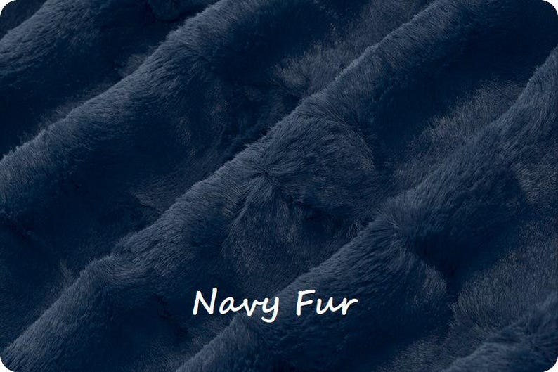 May include: Close-up of navy blue faux fur fabric. The plush material has a soft, textured appearance with visible fibers and folds. The words "Navy Fur" are written in white cursive across the bottom of the image.
