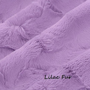 May include: A soft, plush fabric in a solid lilac color with a dense, shaggy texture. The material features deep folds and ripples that create natural shadows across the surface. The text "Lilac Fur" is printed in black in the bottom corner.