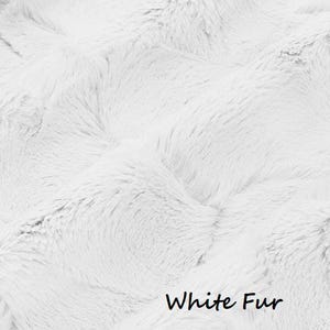 Pu&ograve; includere: Primo piano di un tessuto di pelliccia bianca con un aspetto morbido e strutturato. L'immagine mostra un materiale denso e soffice con un motivo ondulato. Le parole "White Fur" sono scritte in nero in basso nell'immagine.