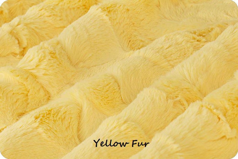 May include: Close-up of a soft, yellow fur fabric. The plush material has a textured appearance with diagonal ridges. The words "Yellow Fur" are printed in black at the bottom of the image. The fabric is likely used for blankets or clothing.