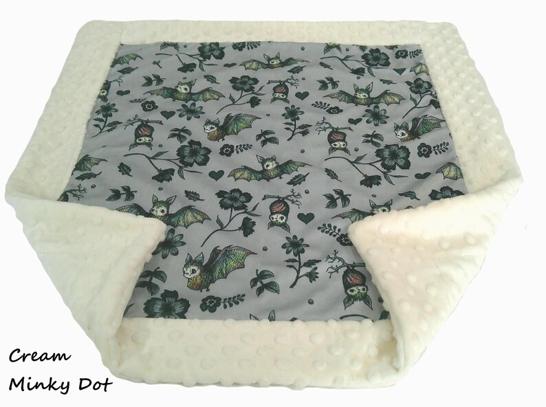 May include: A square blanket featuring a central gray panel with a repeating pattern of bats, flowers, and hearts. The blanket is bordered by a textured cream-colored minky dot fabric. The text Cream Minky Dot is visible in the bottom left corner.