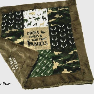 May include: A brown and green patchwork baby blanket with a soft, plush border. The blanket features various patterns, including camouflage, deer antlers, and arrows. The center panel has the text "DUCKS TRUCKS & EIGHT POINT BUCKS".