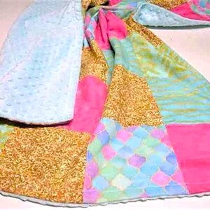 May include: A patchwork baby blanket with a soft, blue minky backing. The blanket features a variety of colorful fabrics, including pink, blue, and gold.