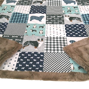 May include: A patchwork quilt featuring various patterns and dog illustrations. The quilt has a brown, plush border. The squares include dog silhouettes, bones, and plaid patterns in shades of blue, white, and gray. The quilt is designed for pets.