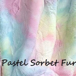 May include: A soft, plush faux fur fabric featuring a tie-dye pattern of blended pastel pink, blue, yellow, and green colors. The surface has a thick, textured pile. The text "Pastel Sorbet Fur" is printed in black across the lower center area.
