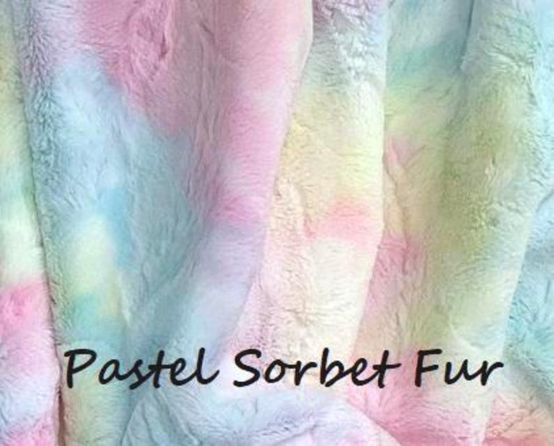 May include: A soft, plush faux fur fabric featuring a tie-dye pattern of blended pastel pink, blue, yellow, and green colors. The surface has a thick, textured pile. The text "Pastel Sorbet Fur" is printed in black across the lower center area.