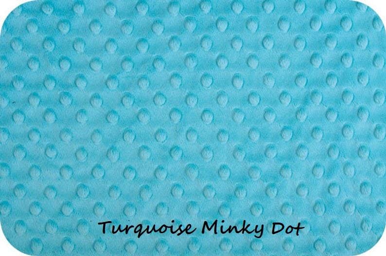 May include: A turquoise minky fabric featuring a raised, embossed dot pattern across the entire surface. The text "Turquoise Minky Dot" is printed in black, sans-serif lettering at the bottom center of the fabric material.