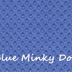 May include: A blue minky fabric featuring a raised, embossed dot pattern across the entire surface. The text "Blue Minky Dot" is printed in white, cursive lettering across the lower portion of the fabric, which has a soft, textured appearance.
