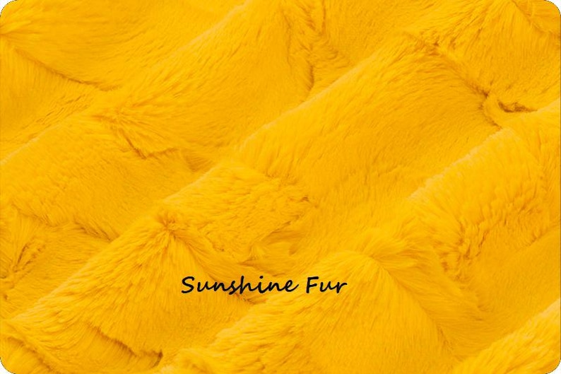 Pu&ograve; includere: Primo piano di un tessuto in finta pelliccia giallo brillante. Il materiale morbido presenta un motivo strutturato e ondulato. Le parole "Sunshine Fur" sono stampate in nero, in minuscolo.