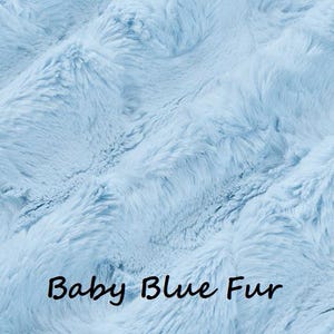 May include: A soft, light blue faux fur fabric with a dense, plush texture and wavy, directional pile. The surface features a consistent baby blue color throughout, with the text "Baby Blue Fur" printed in black in the lower center area.