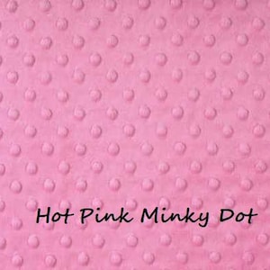 May include: A hot pink minky fabric featuring a raised, embossed dot pattern across the entire surface. The text "Hot Pink Minky Dot" is printed in black, sans-serif lettering near the bottom center of the fabric, which has rounded corners.